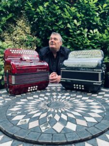 london irish button accordion player Andy Martyn outside in garden with one red accordion and one black accordion