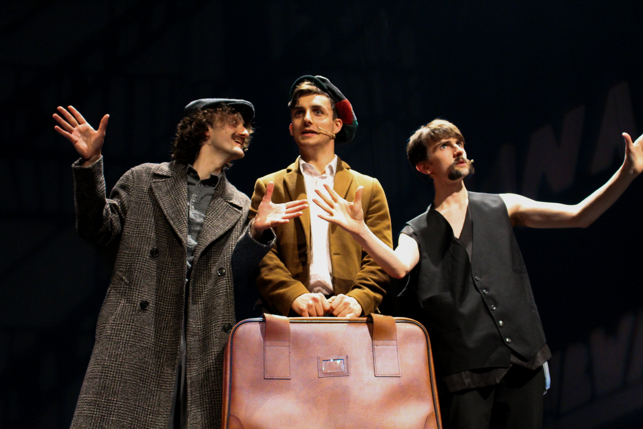 3 men in dramatic scene with the man in the centre holding a suitcase