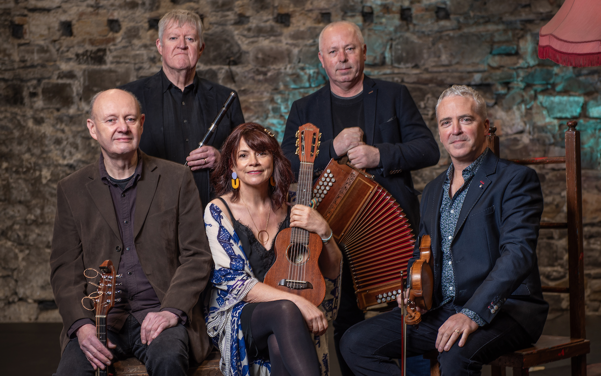 Dervish irish musicians looking at the camera in front of a wall with their instruments