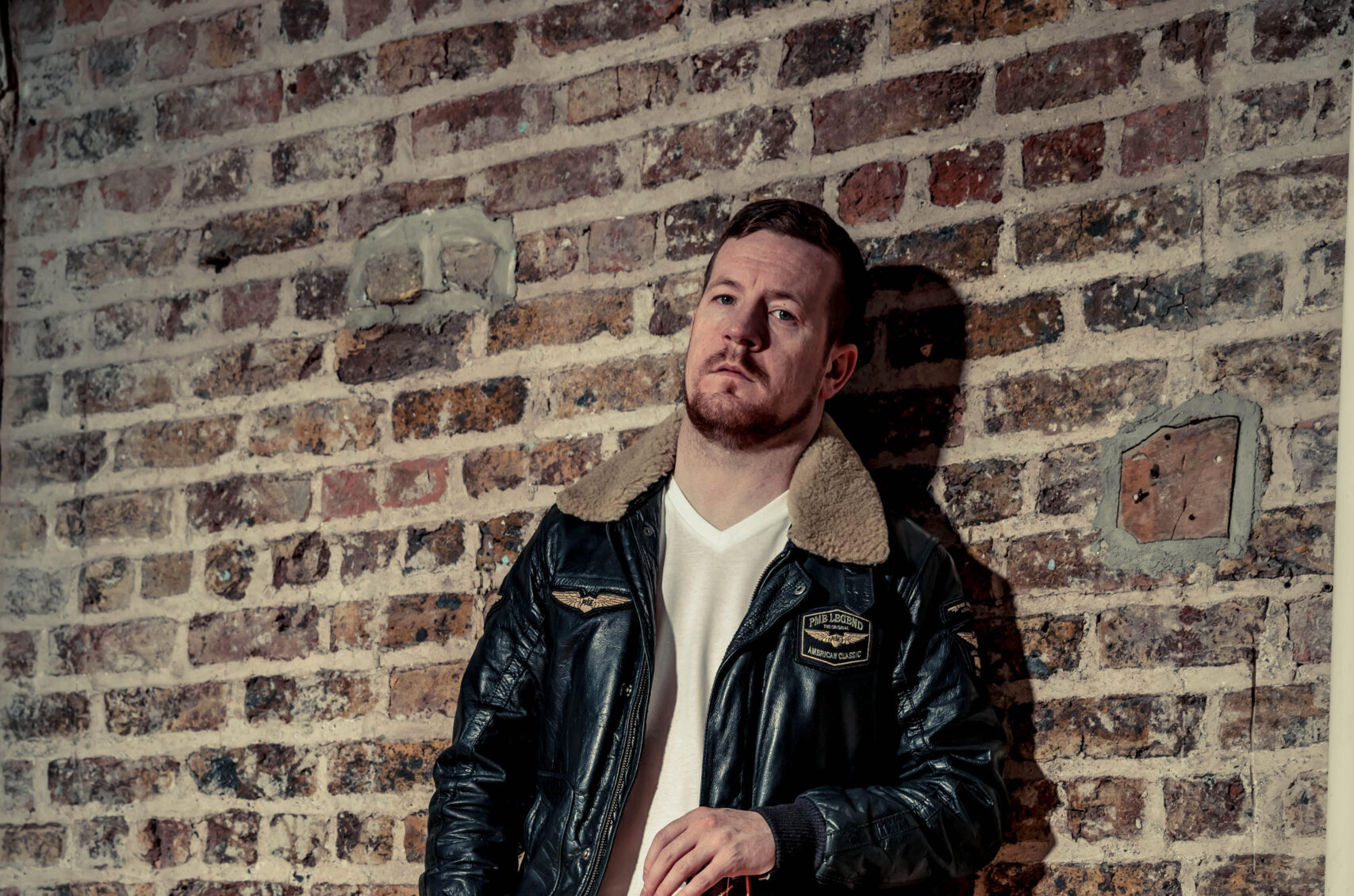 Irish musician George Murphy by a brick wall with a guitar in hand